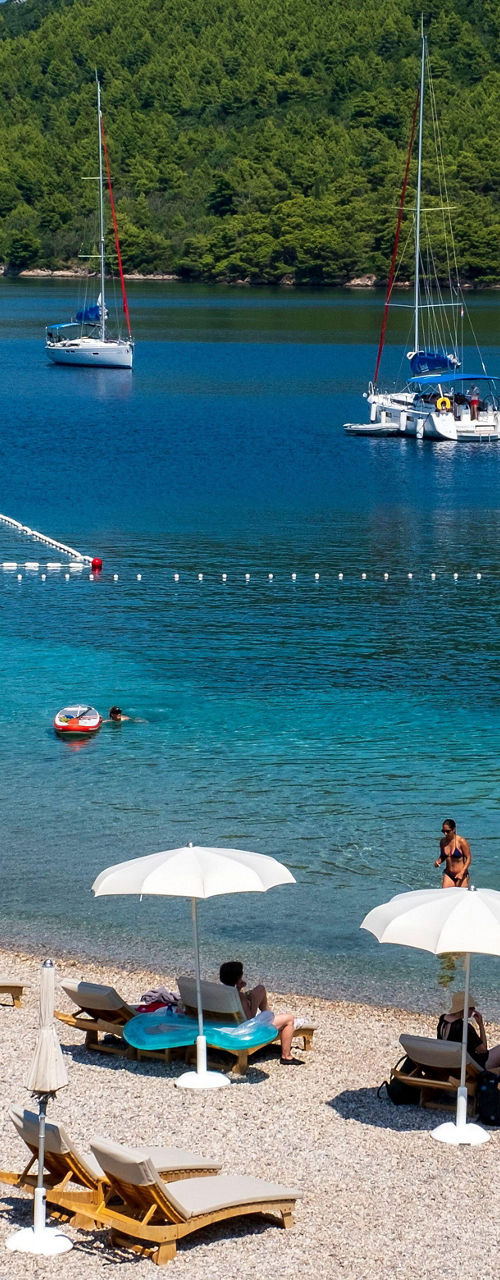 Sunny pebble beach with umbrellas and anchored sailboats