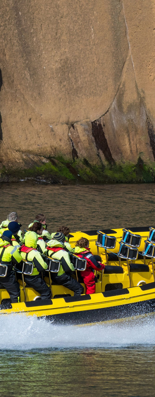 Yellow speedboat with passengers near rocky cliffs