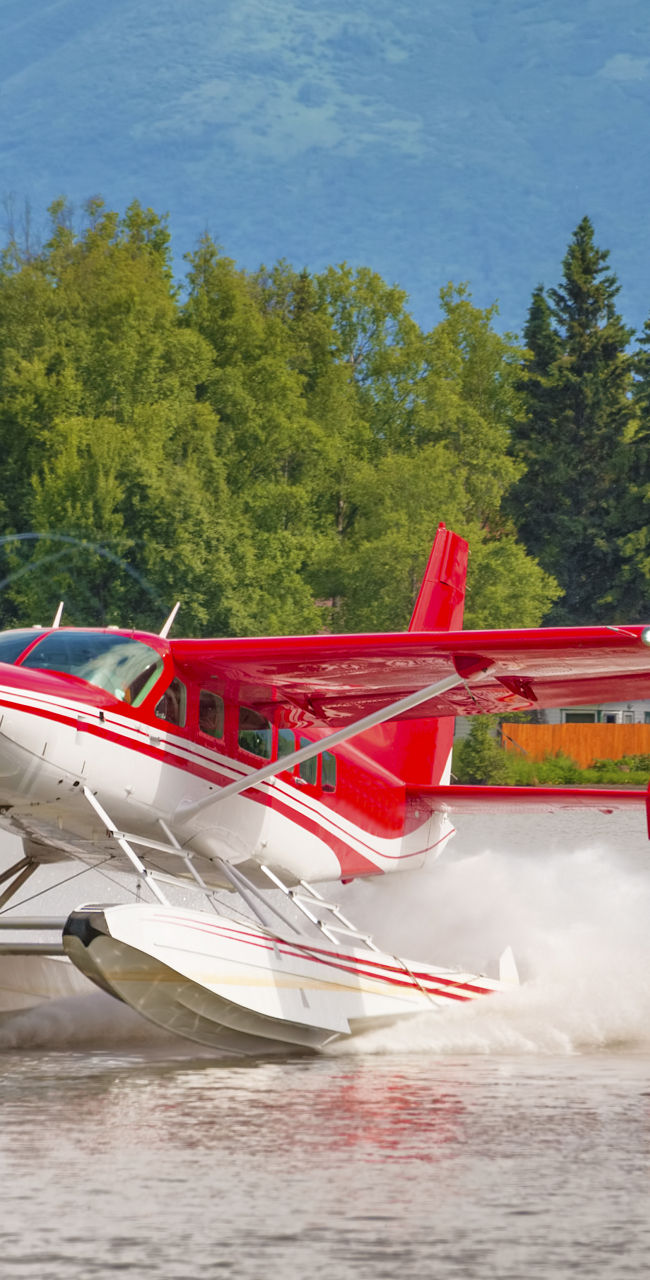 Red seaplane landing on calm lake