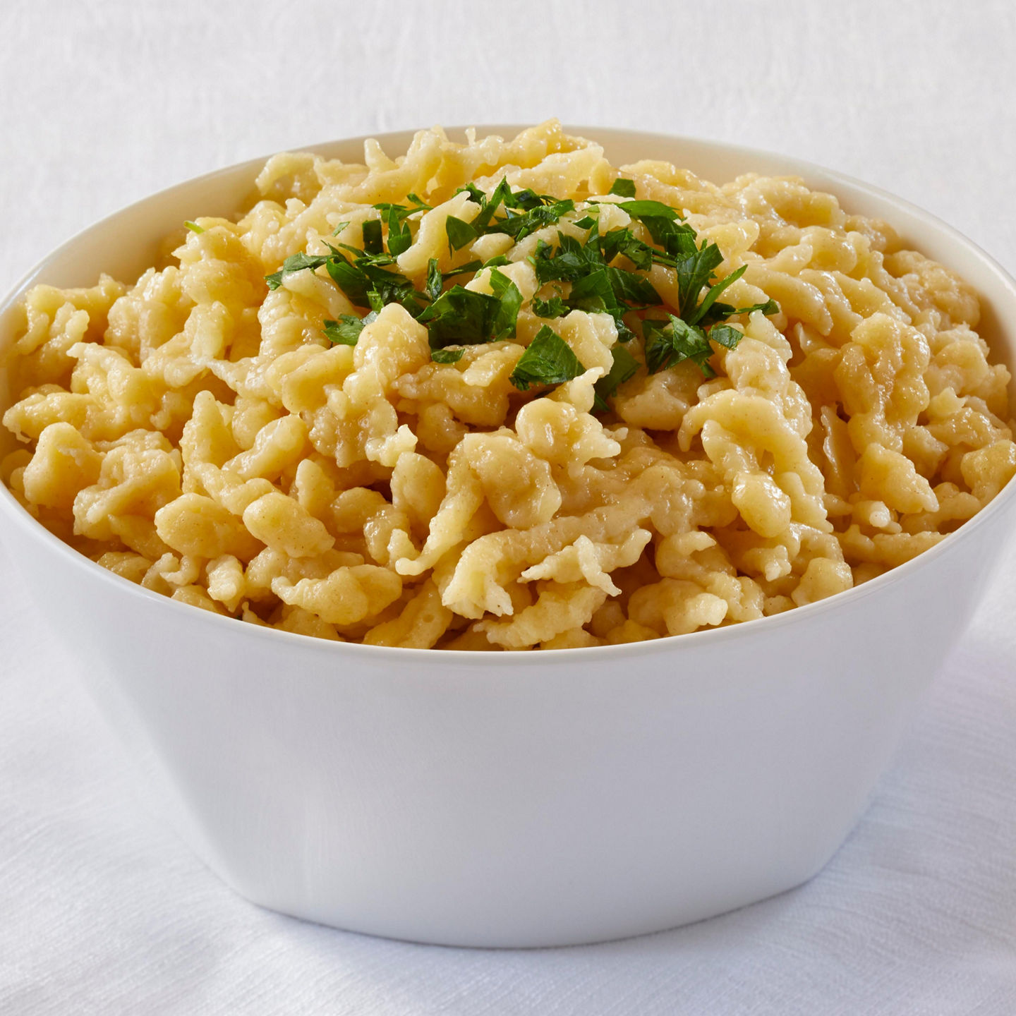 Bowl of cheesy spaetzle with parsley garnish