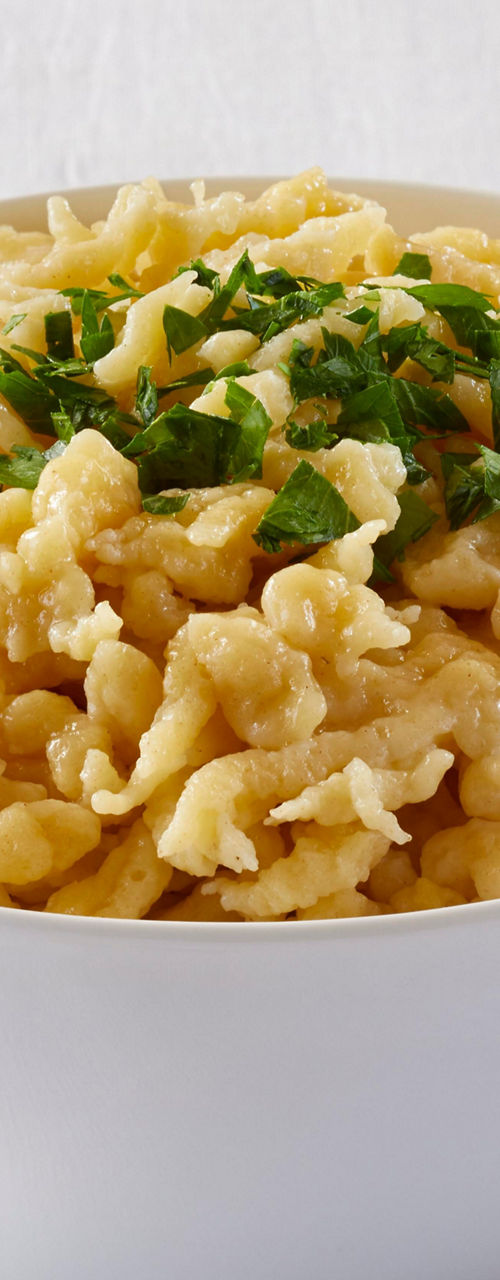 Bowl of cheesy spaetzle with parsley garnish