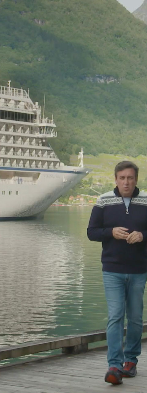 Man walking on dock near large cruise ship in fjord