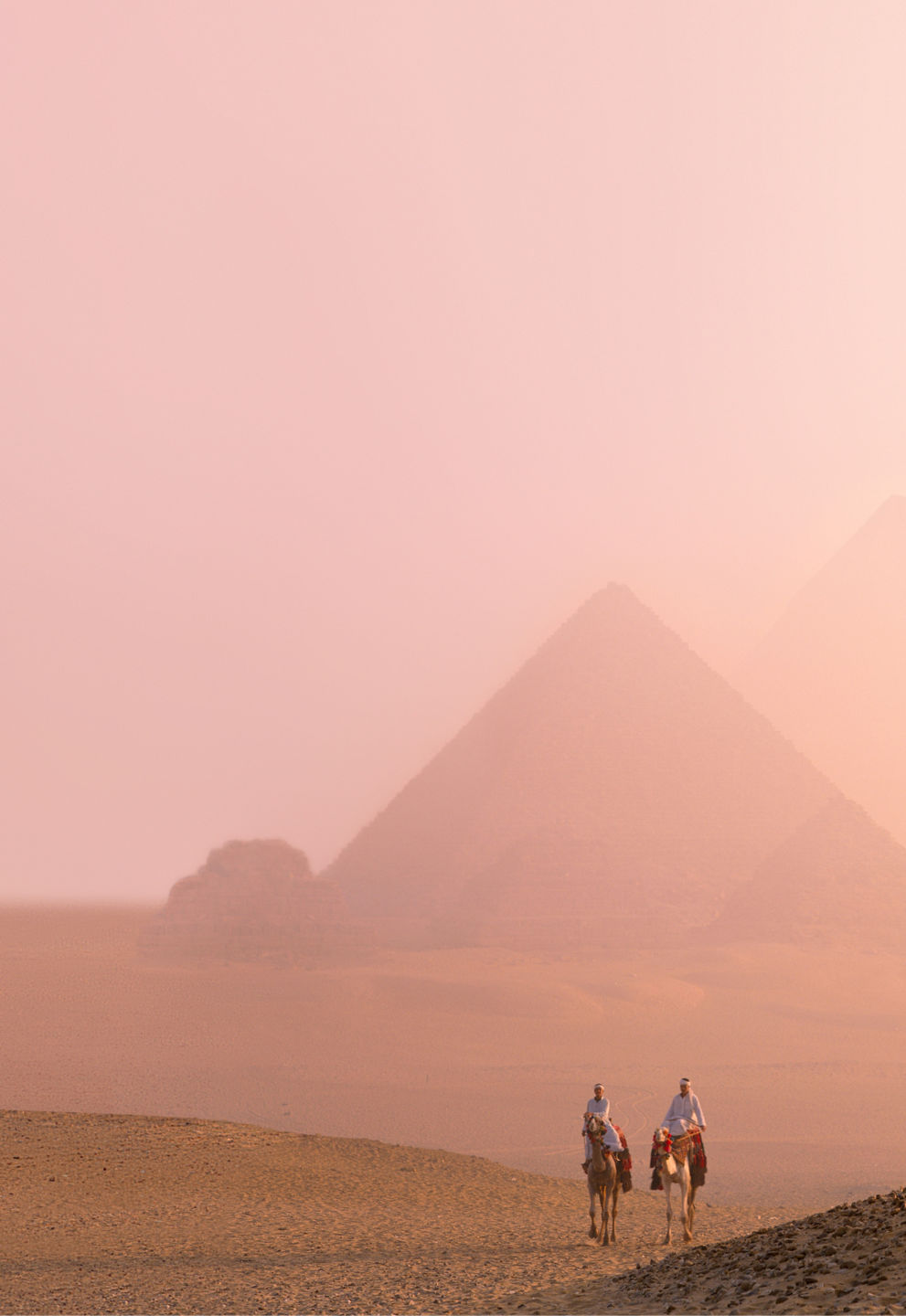 Camel riders near pyramids at sunset