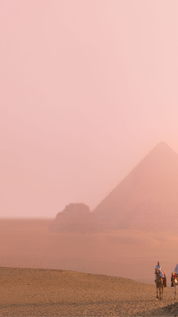 Camel riders near pyramids at sunset