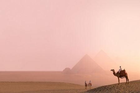 Camel riders near pyramids at sunset