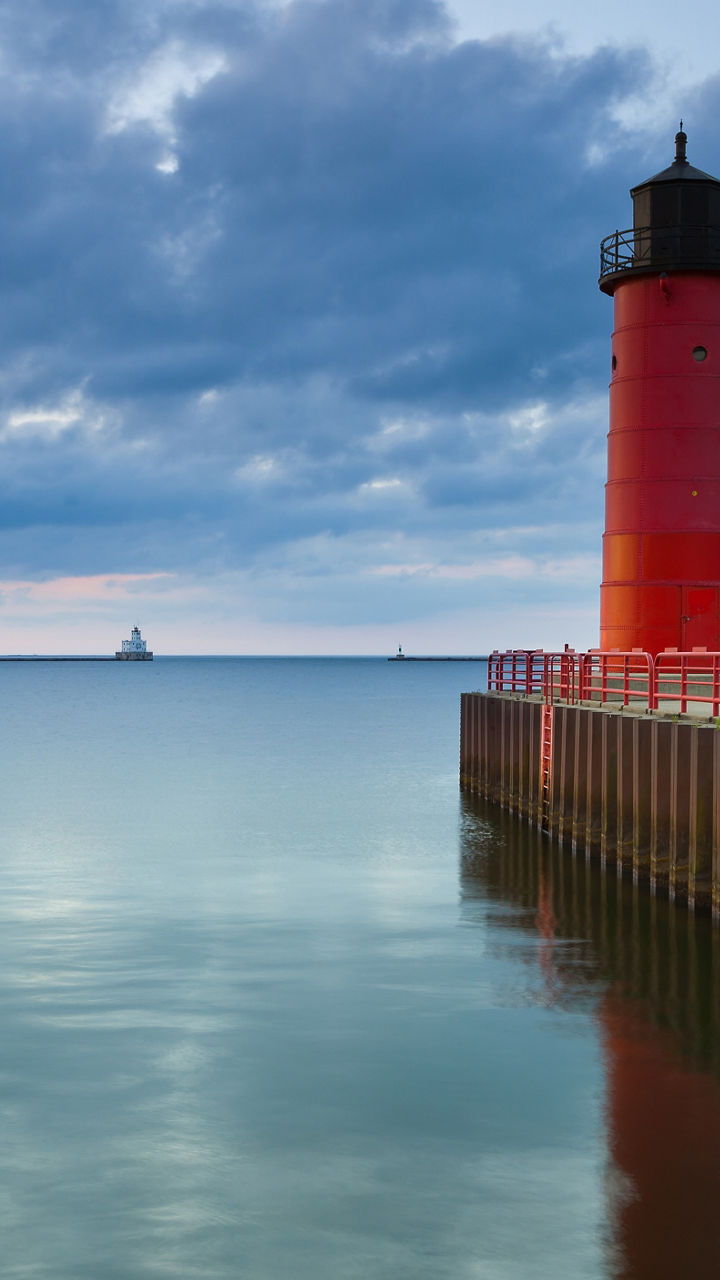 Red lighthouse by calm waters at sunset