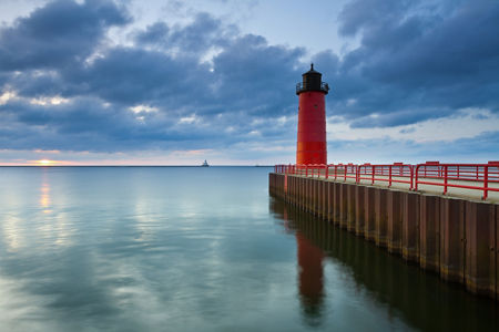 Red lighthouse by calm waters at sunset