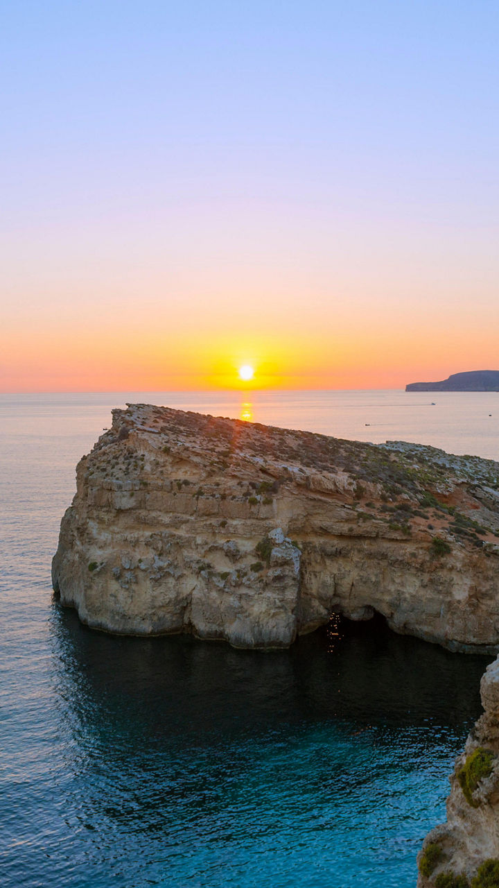 Sunset over rocky coastal cliffs and boats