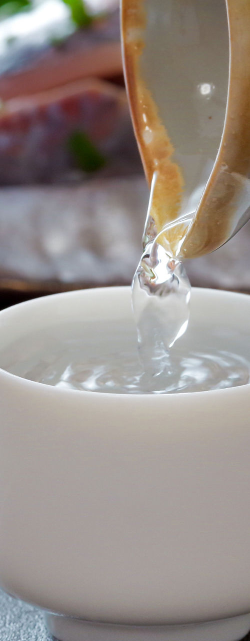 Pouring sake into ceramic cup with sashimi background