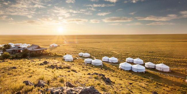 Sunlit Mongolian yurts in vast grassland