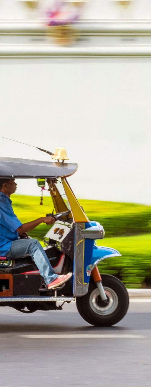 Tuk-tuk driving past urban greenery