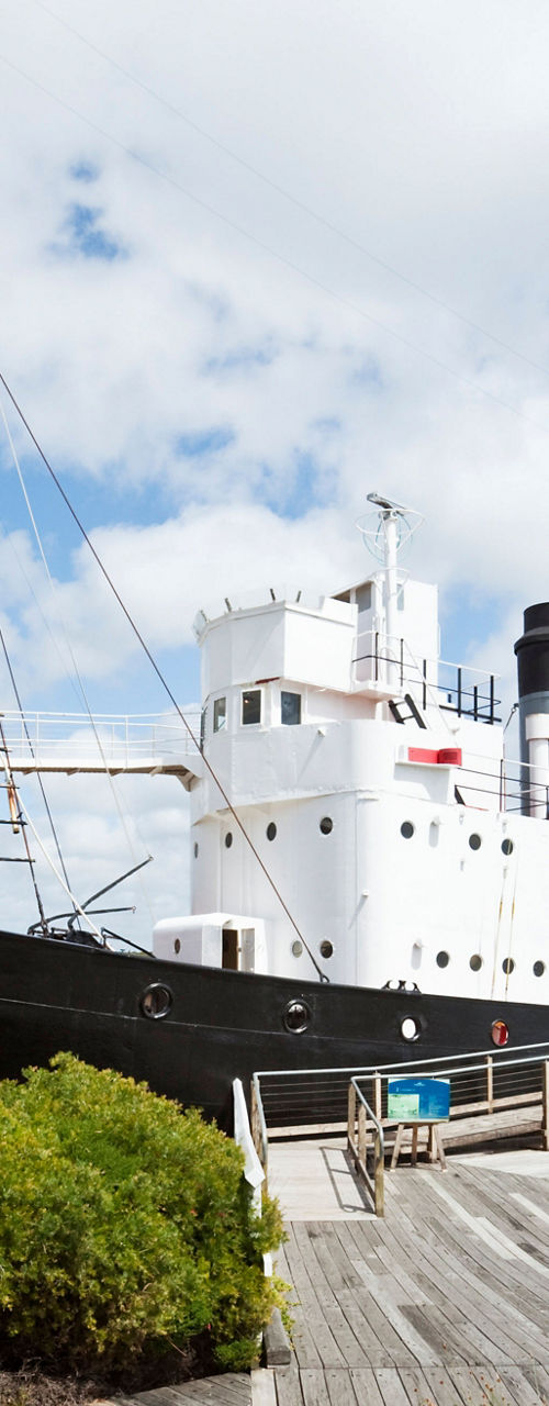 Historic ship docked by scenic boardwalk