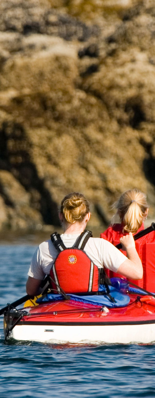 Two women kayaking near rocky shoreline