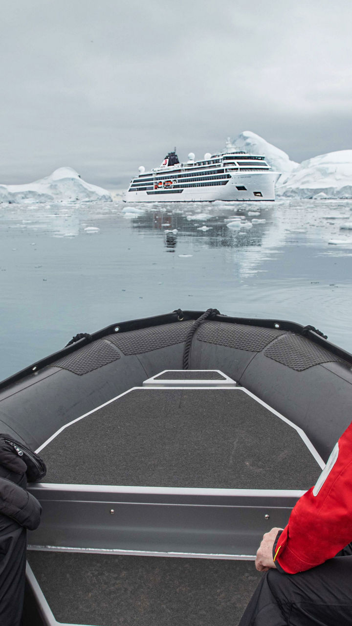 Explorers in inflatable boat near icy cruise ship