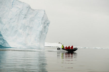 Iceberg with boat and explorers in Arctic waters